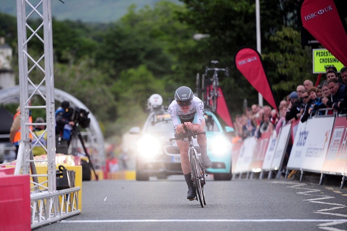 cyclist crosses the line with support vehicles behind
