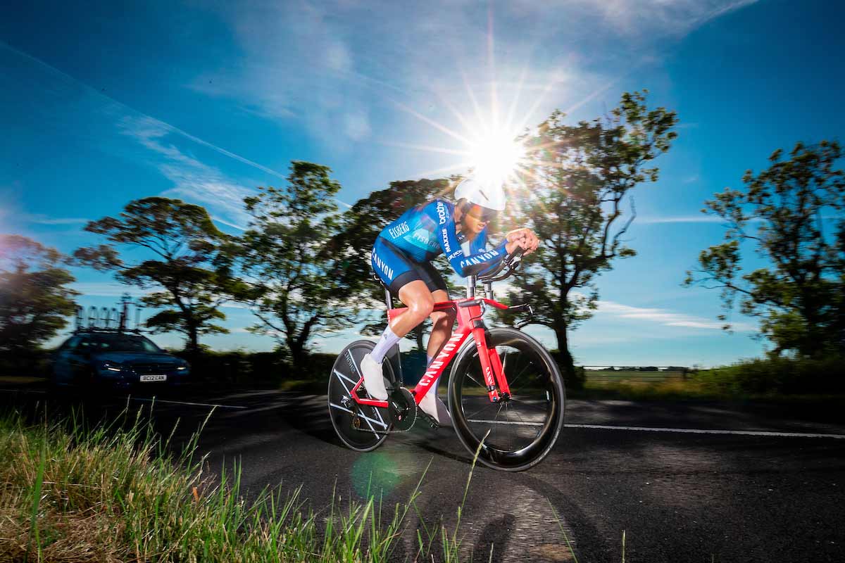 Harry Tanfield cycling on a road with a support car behind him