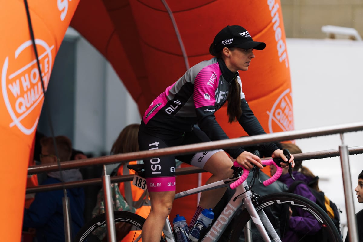 Side shot of cyclist Rebecca Durrell on her bike wearing the Brother UK-Tifosi p/b OnForm team kit