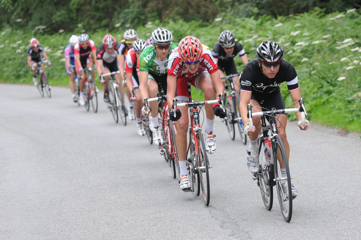 Cyclist Dean Downing leading a group of cyclists as they approach the camera while riding up a hill with greenery in the background