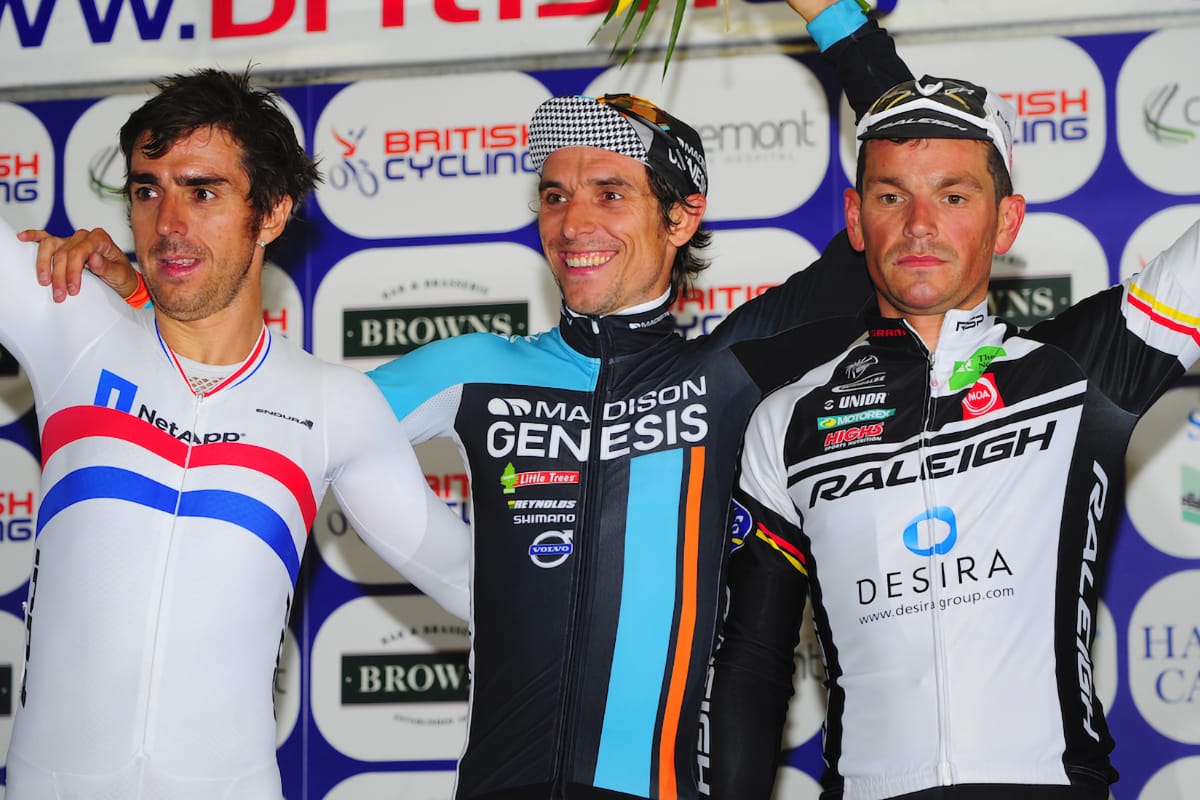 Dean Downing, Russell Downing and Graeme Briggs celebrating victory on a podium with sponsorship logos in the background