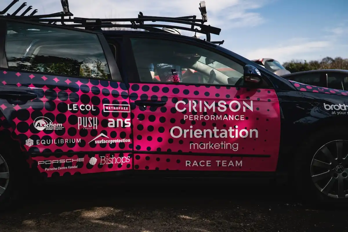 Side view of a black Crimson Performance race team support vehicle with pink sponsor livery