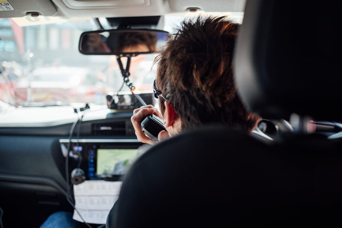Cherie Pridham talking on a CB radio viewed from the back seat of a cycling team support vehicle