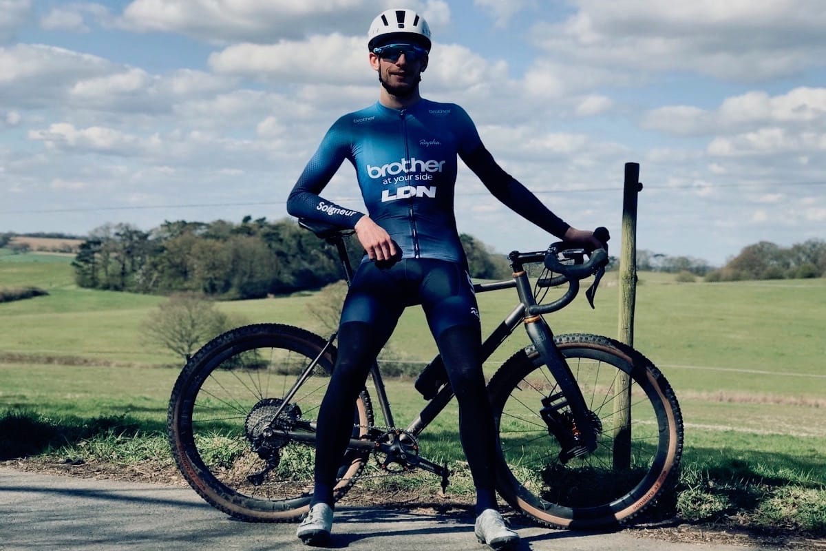 Cyclist Tim Allen standing in front of his bike at the side of a country road with green fields in the background