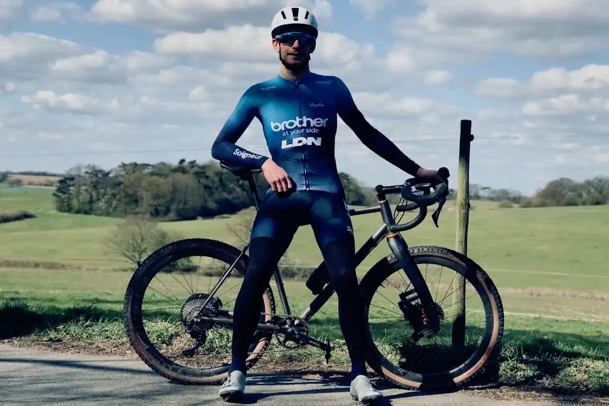 Cyclist Tim Allen standing in front of his bike at the side of a country road with green fields in the background