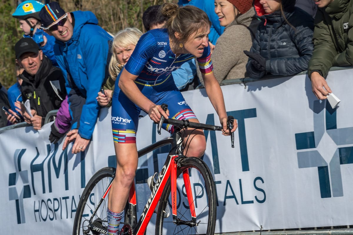 Cyclist Rebecca Richardson looking determined as she approaches the finish line of a hill climb with spectators in the background