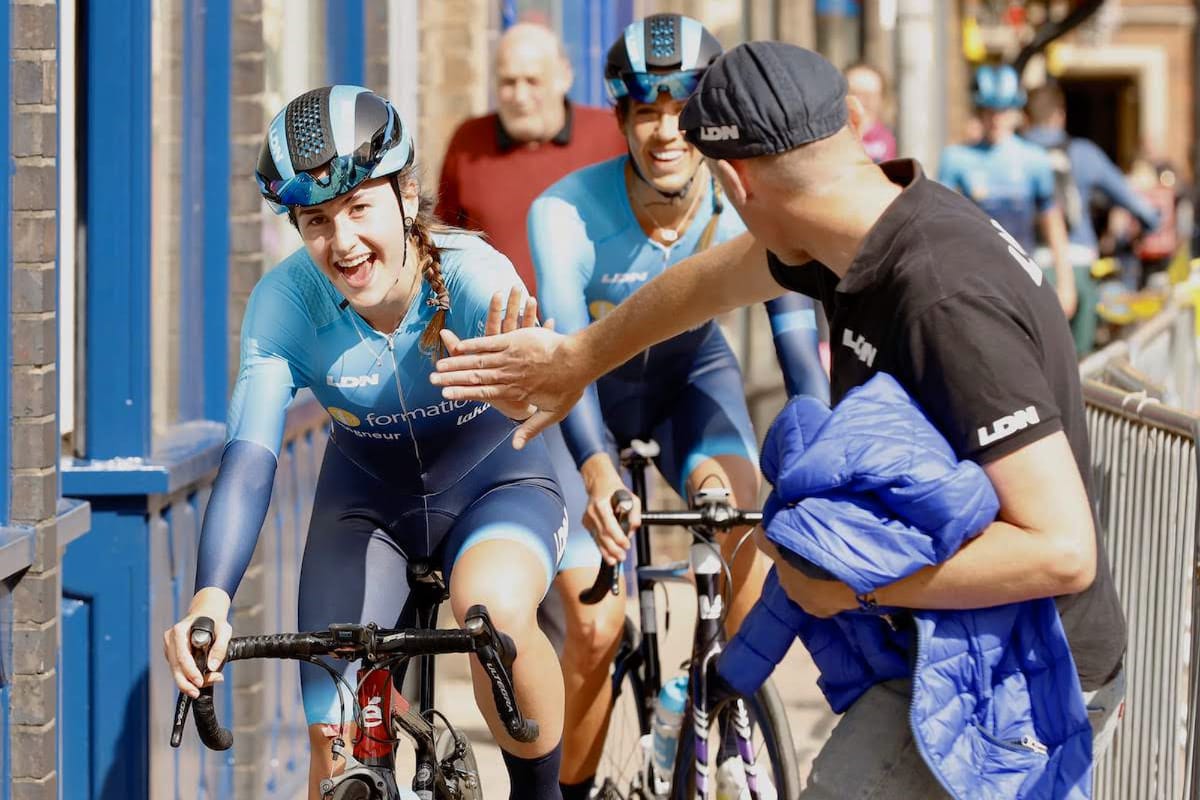 General manager Ian Watson of Team Brother UK-LDN giving a high five to a cyclist as she passes between the side of a building and railings