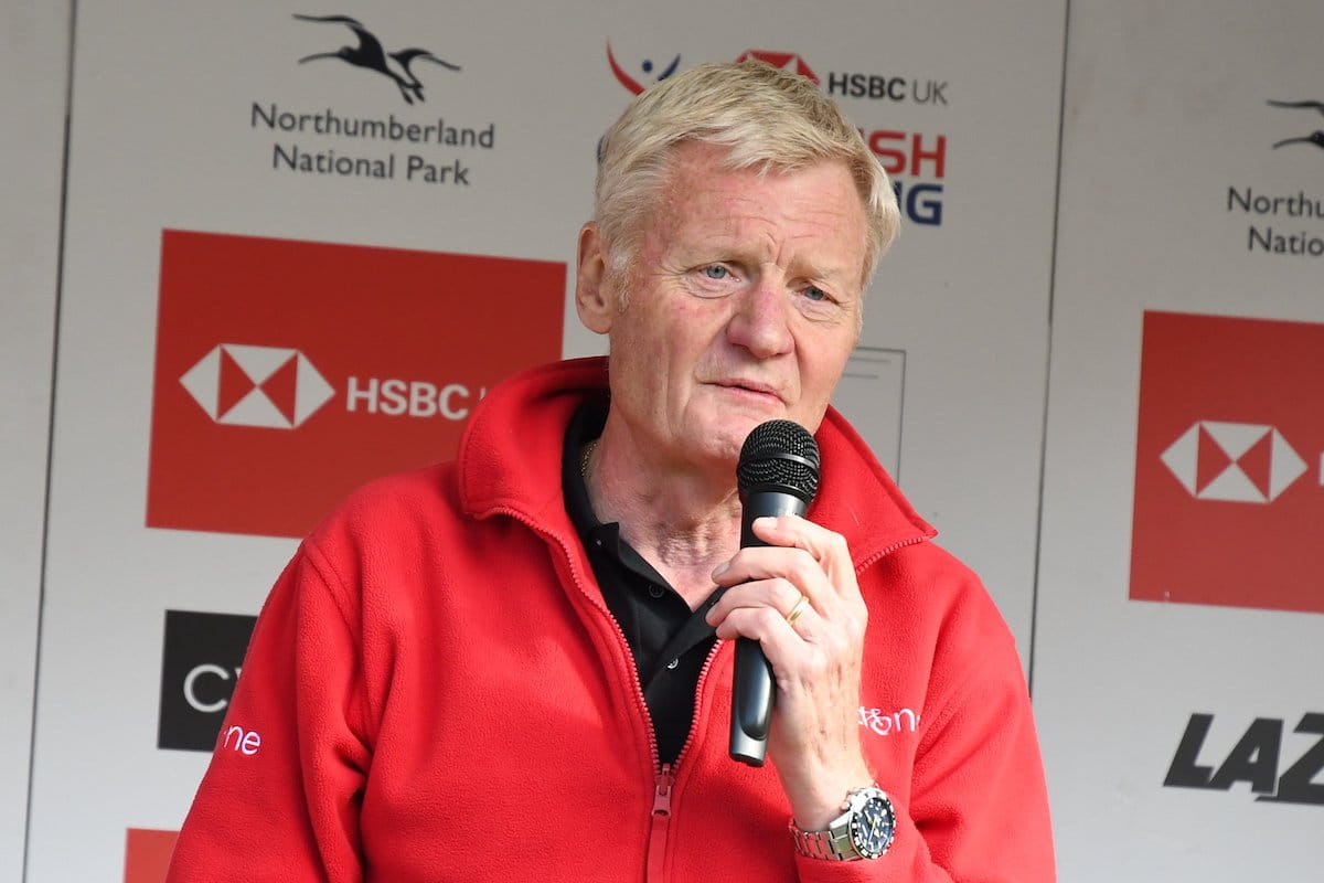 Peter Harrison of Gosforth Road Club speaking into a handheld microphone with sponsorship logos in the background