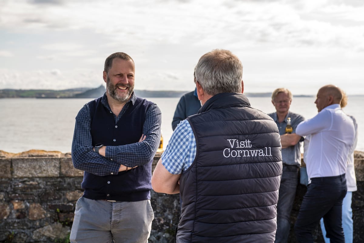 Jonathan Durling partnerships director at The SweetSpot Group standing in from of a stone wall and an expanse of water while talking to someone who has his back to the camera