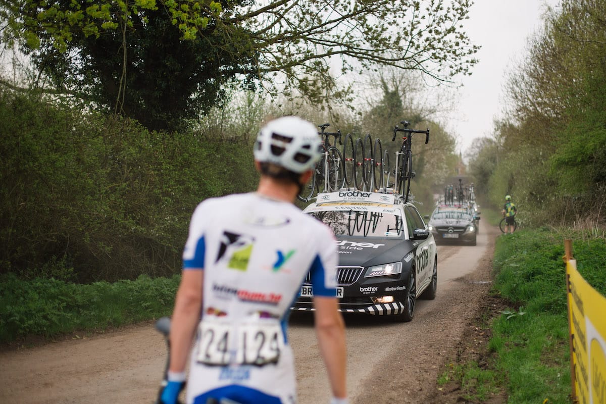 Cyclist holding bike at roadside waiting for oncoming neutral race support vehicles