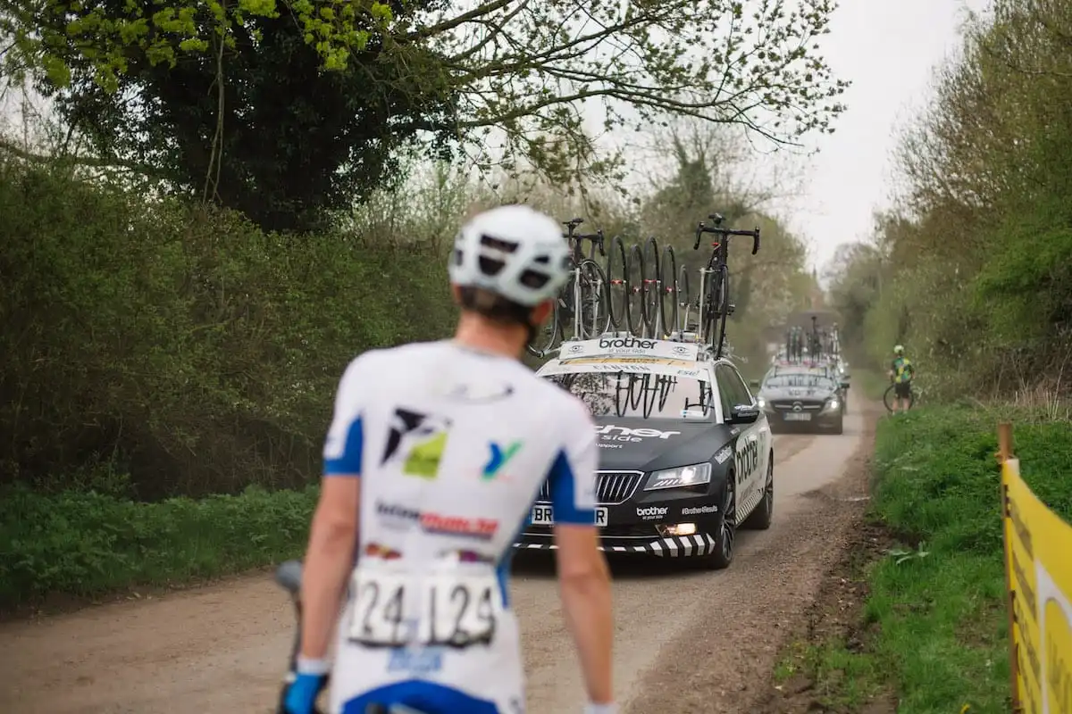 Cyclist holding bike at roadside waiting for oncoming neutral race support vehicles