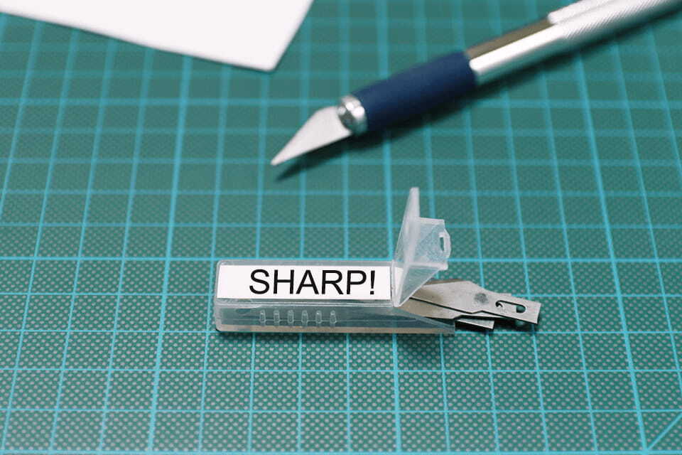 Brother TZe-S221 strong adhesive tape cassette - black on white - warning sharp on scalpel blade packaging saying "SHARP!"