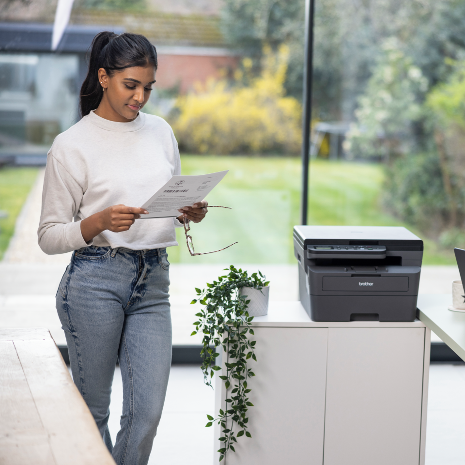 <p>Woman viewing duplex mono output next to DCPL2622DW</p>