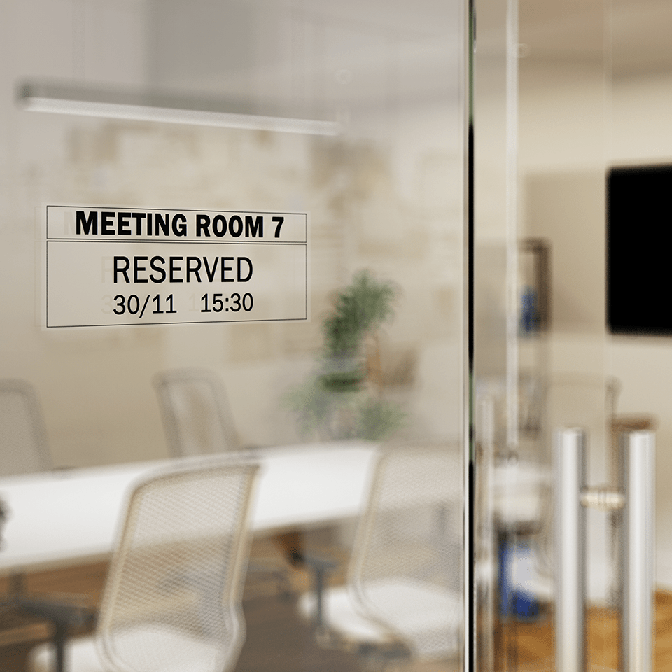 Black on transparent Brother DK film label attached to meeting room glass, with details of meeting room.