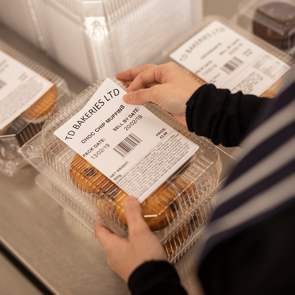 Female wearing apron putting food ingredients label to box of cupcakes