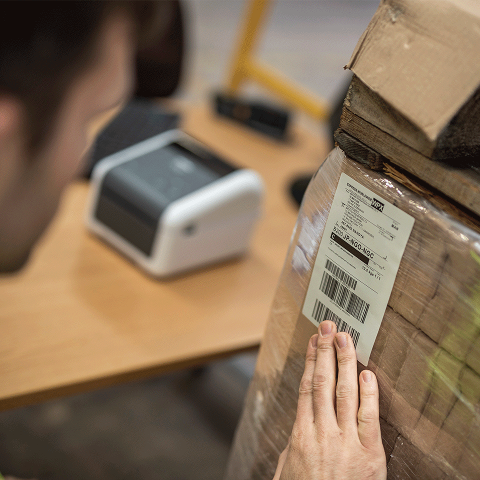 Man putting shipping label on large brown box with Brother TD-4420DN desktop label printer in background