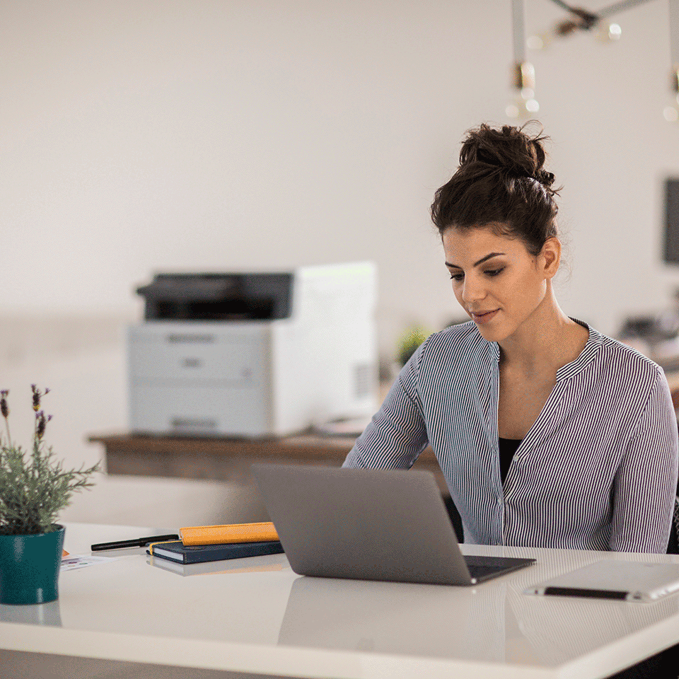 Woman sat at desk using laptop with DCPL3510CDW on table