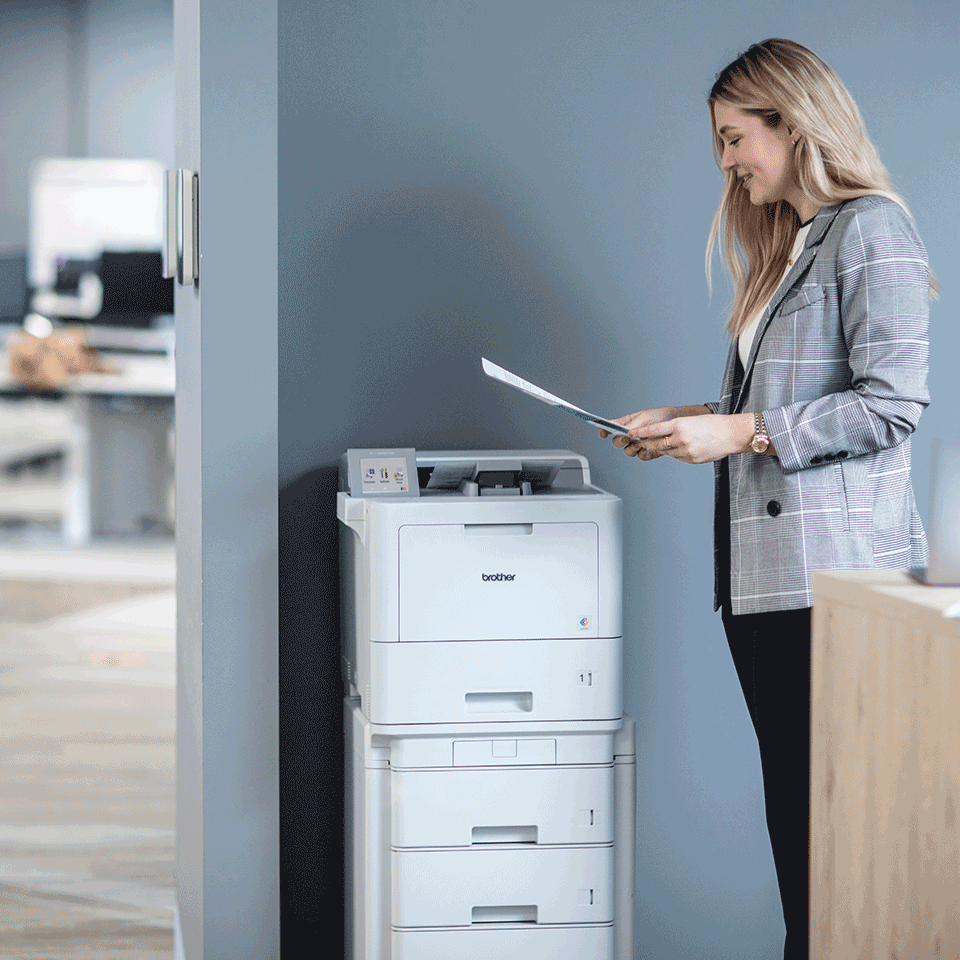 Woman with long blond hairin office holding documents in hand next to floorstanding printer