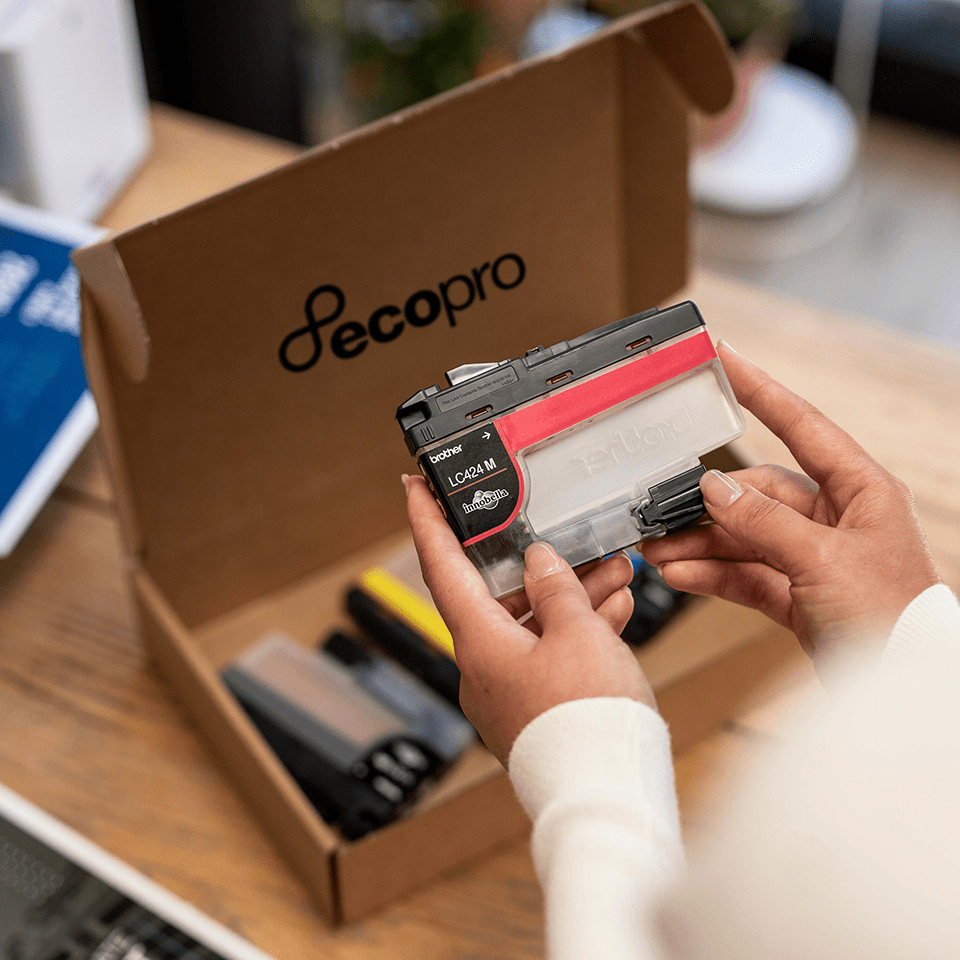 Woman's hand holding magenta ink cartridge over cardboard EcoPro box