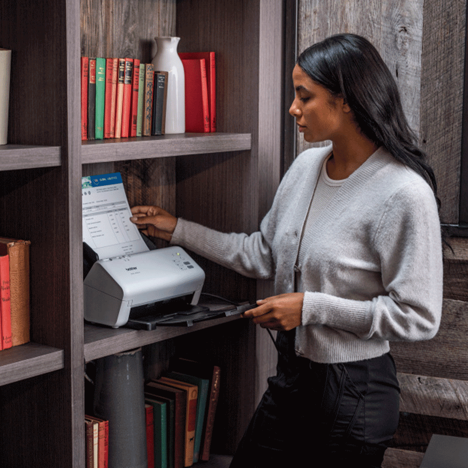 Female stood next to scanner holding document in ADS-4300N, books, shelving