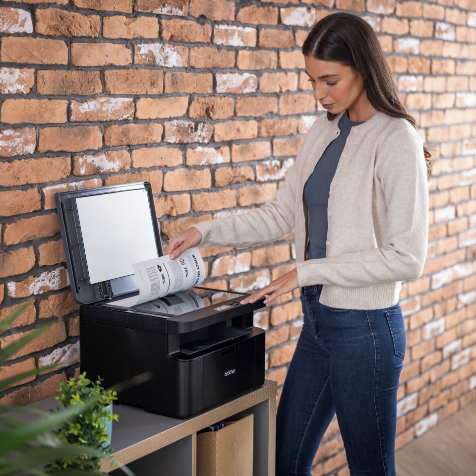<p>Woman placing mono output on the flatbed of the DCP-L1642W laser printer</p>