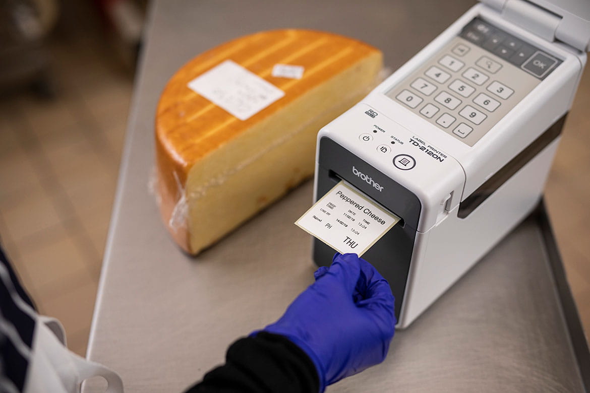 Gloved hand taking food label from Brother TD printer in kitchen