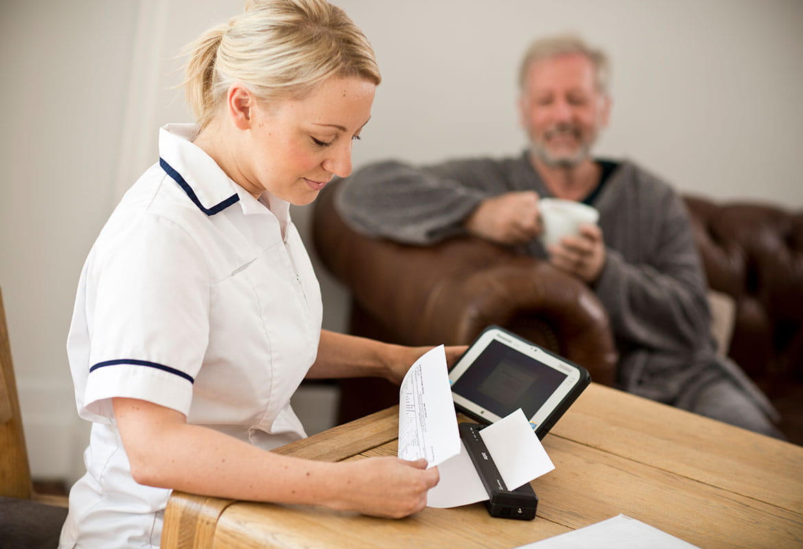 Infirmière assise à une table, imprimant des notes de patients sur une imprimante Brother PJ.