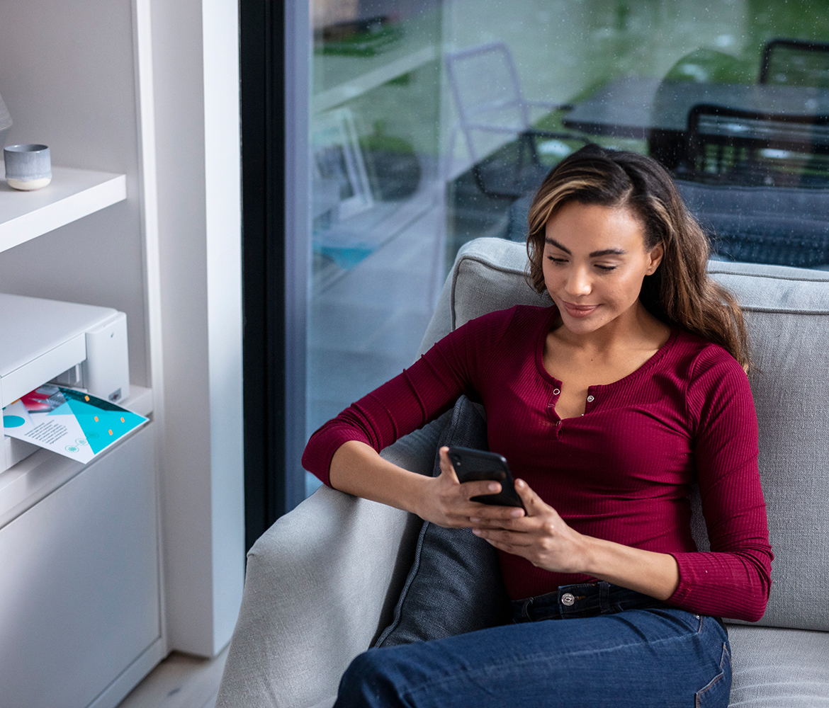 Woman sat on sofa next to a printer looking at her phone