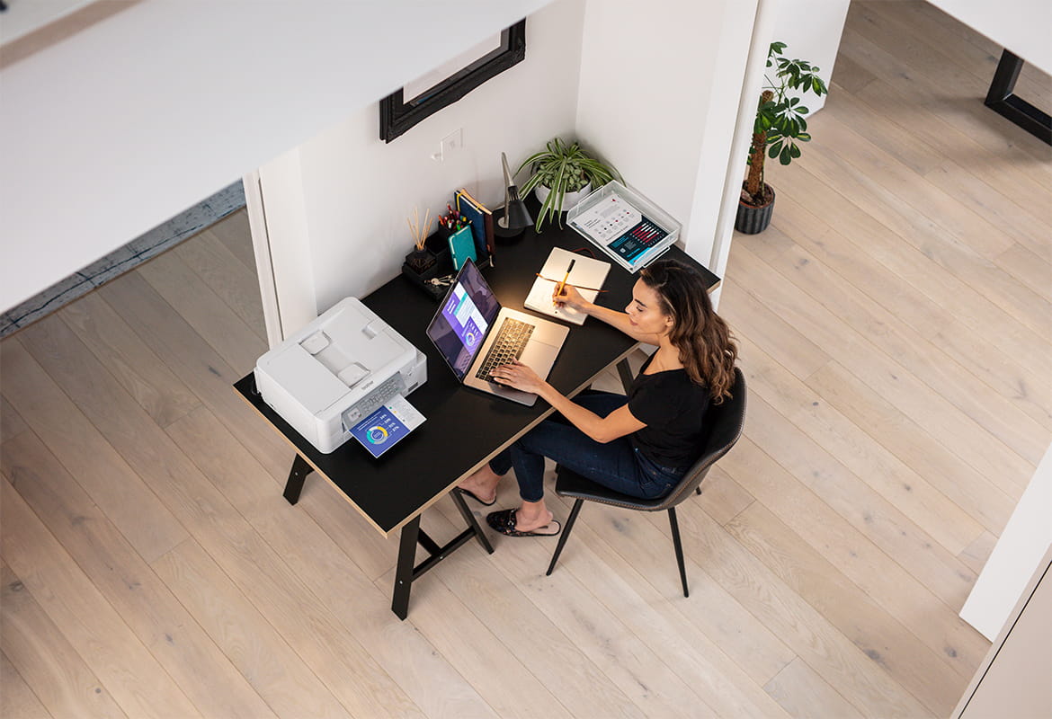 Woman sat at a desk looking at a laptop with a printer by the side