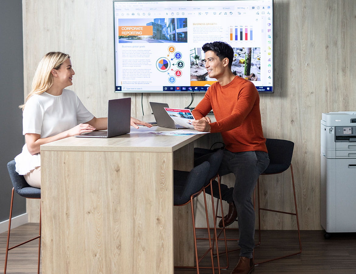 Man and woman sat around high with TV on the back wall and printer