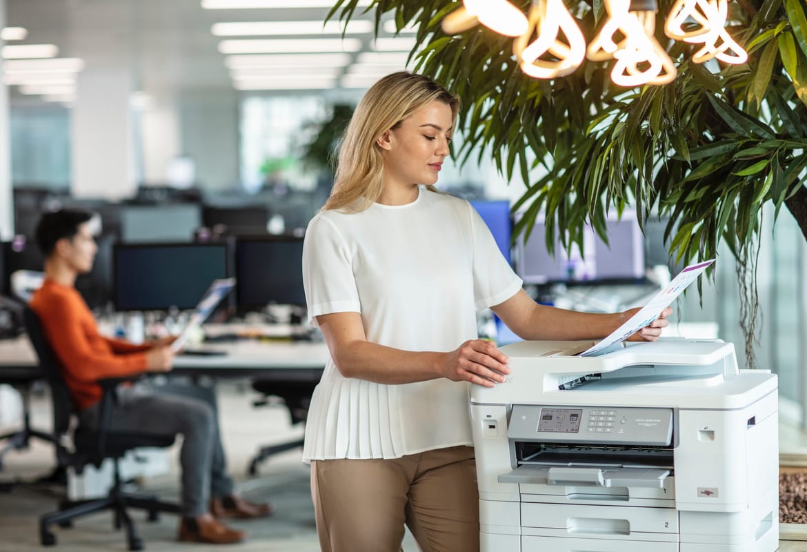 Business woman leaning on a Brother printer while checking a printed document in an SMB office environment