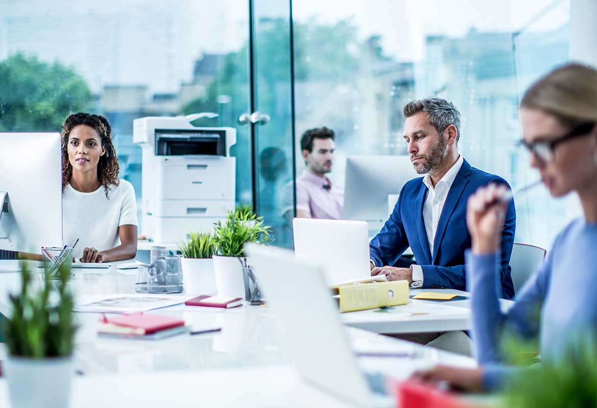 Three people sat at desks in office with a printer