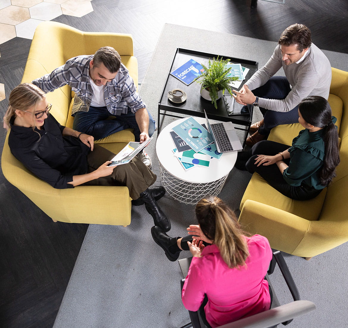 Two men and three women sat around a table, laptop, plants, documents