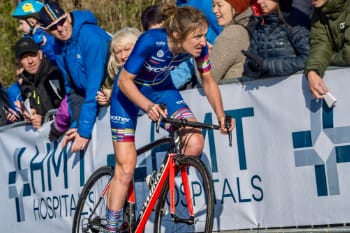 Cyclist Rebecca Richardson looking determined as she approaches the finish line of a hill climb with spectators in the background