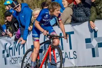 Cyclist Rebecca Richardson looking determined as she approaches the finish line of a hill climb with spectators in the background