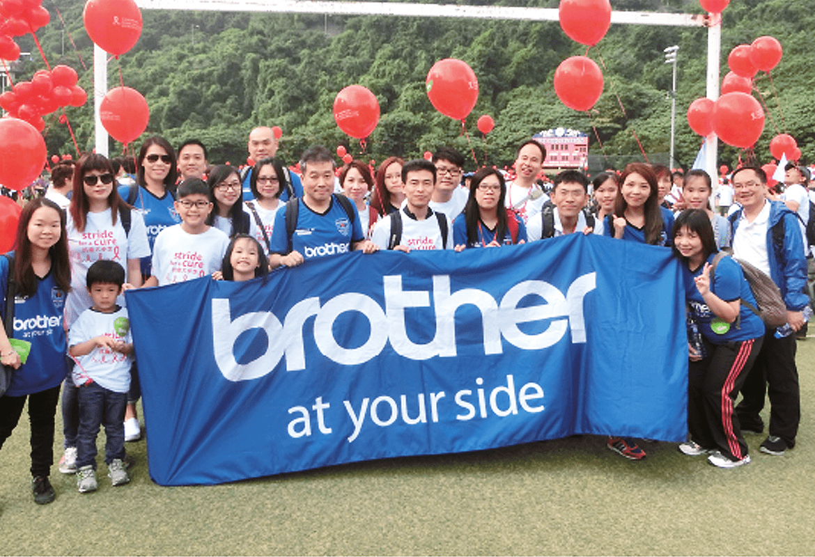 Crowd of people holding a Brother banner with red balloons in the background