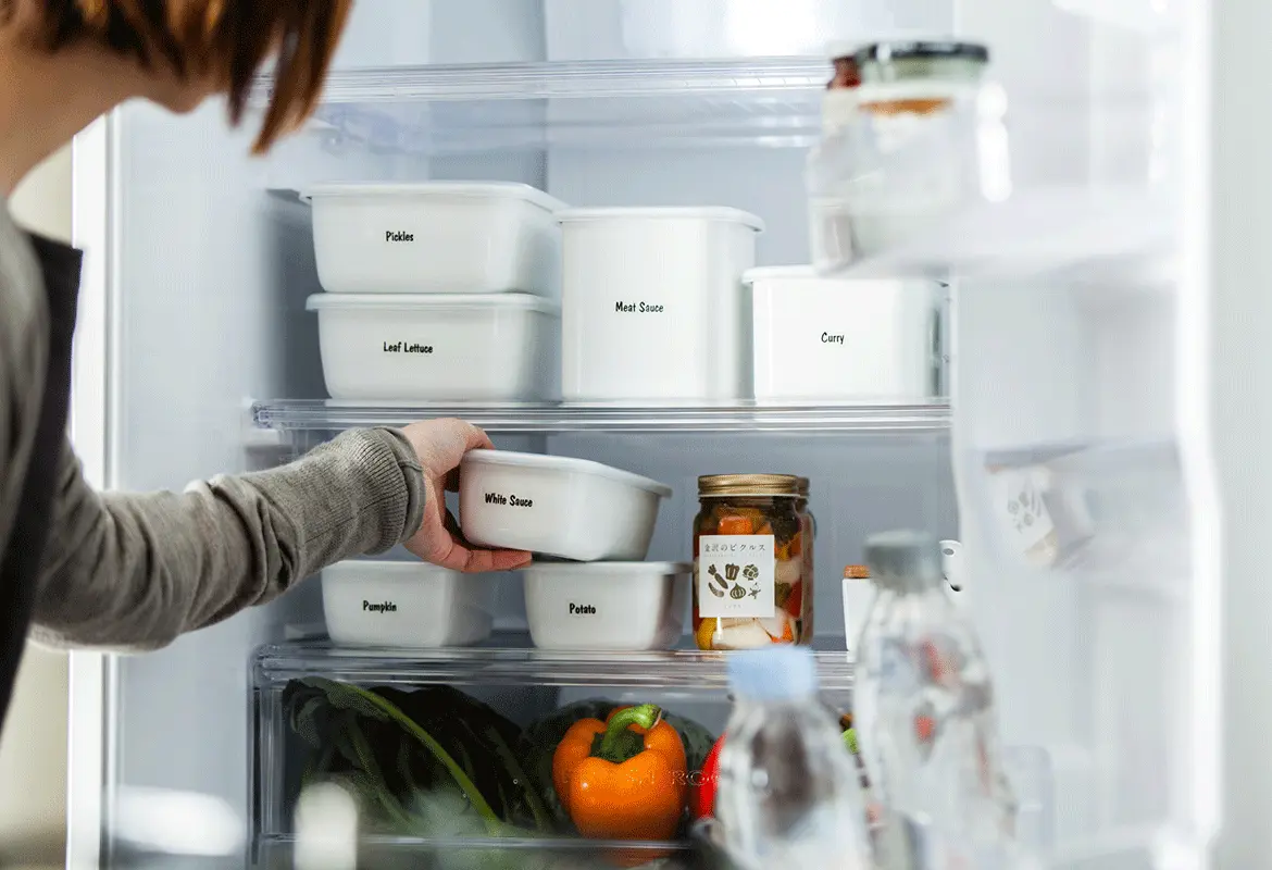 A woman puts white food containers marked with white labels with black writing in a refrigerator