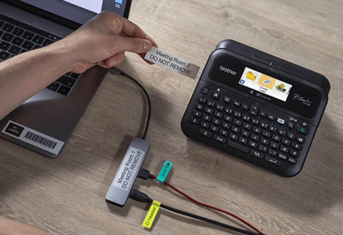 P-touch label printer on an office desk, connected to a laptop, with a label printing