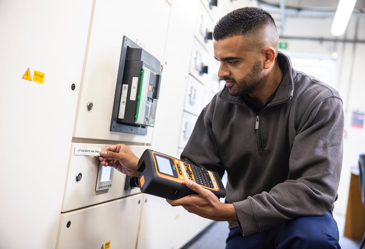 An electrician applying a label to an electrical panel on-site, having used a Brother P-touch E-series label printer