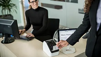 A woman removing a visitor pass from a label printer at a reception desk