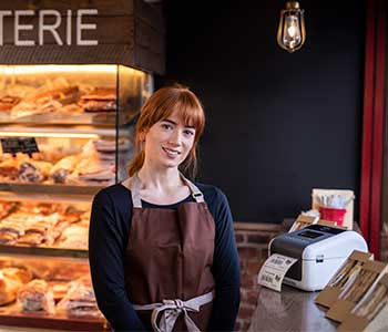 Woman wearing brown apron in cafe with sandwiches and TD label printer