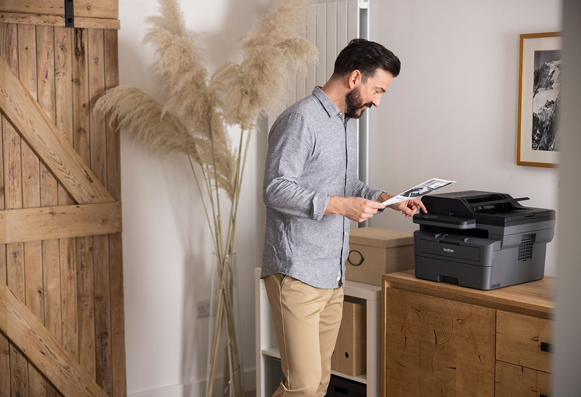 Un homme debout chez lui utilisant l’écran tactile de son imprimante Brother