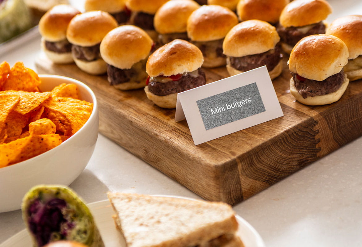 Plate of sandwiches, mini burgers on table with white and silver food tend card