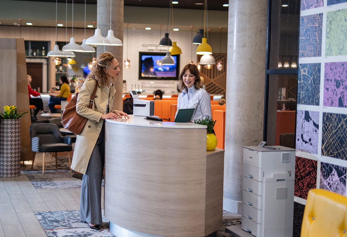 Receptionist with guest at reception, printer, lights, restaurant, flowers, chair