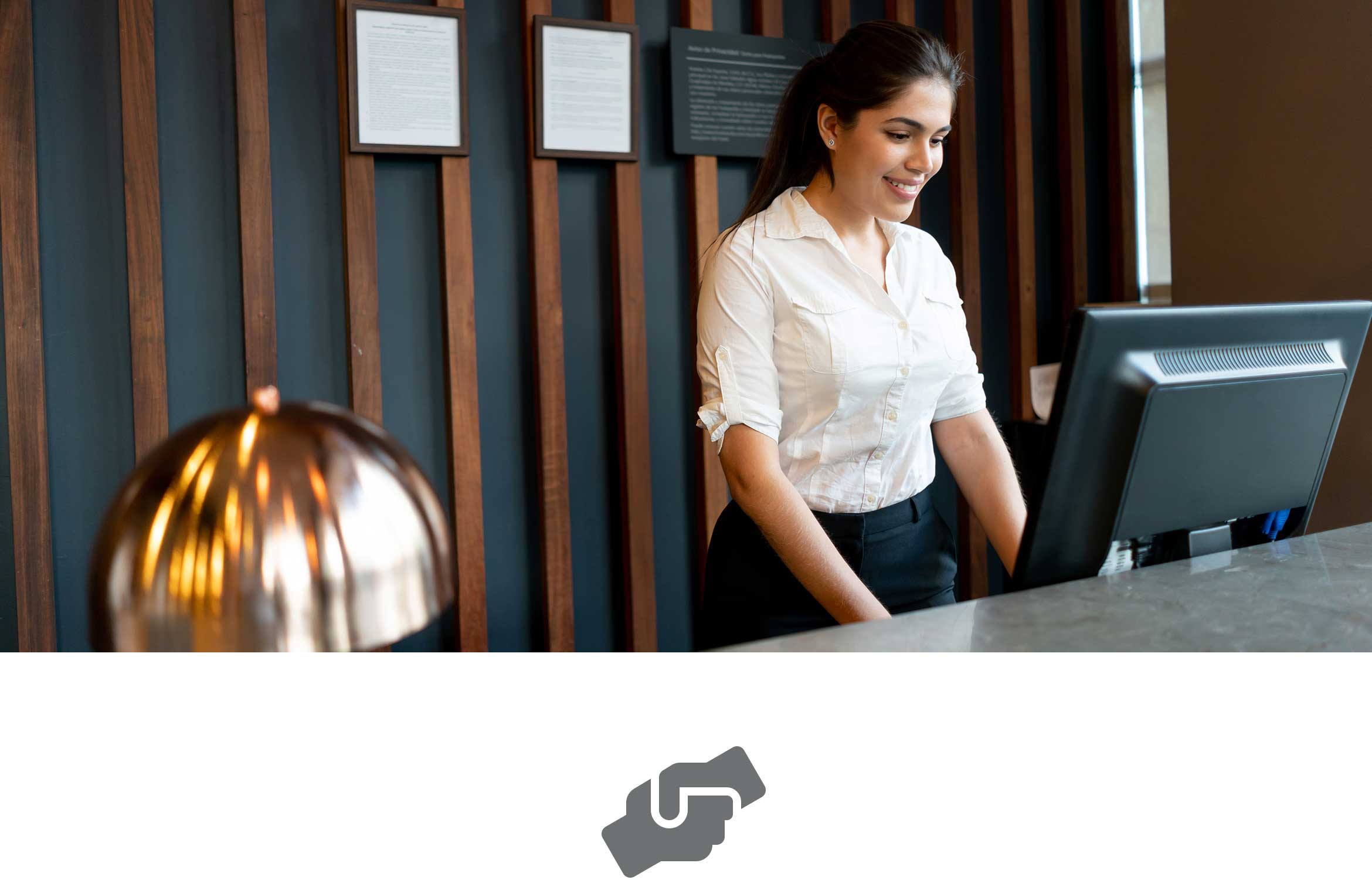 Female receptionist with dark hair tied back wearing white shirt holding at reception using computer