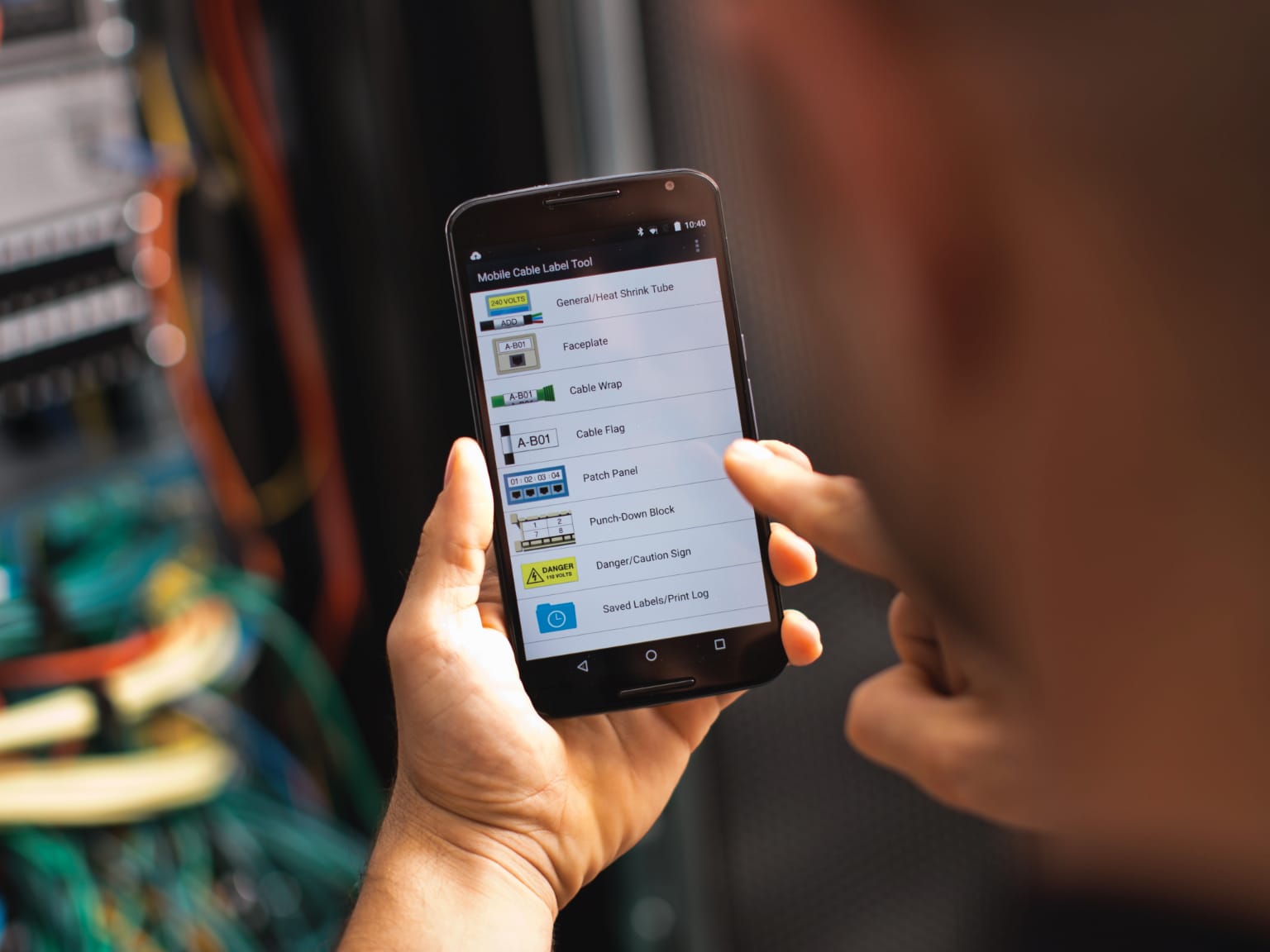 Electrician using the Mobile Label Cable Tool app on a smartphone with electrical cabling in the background