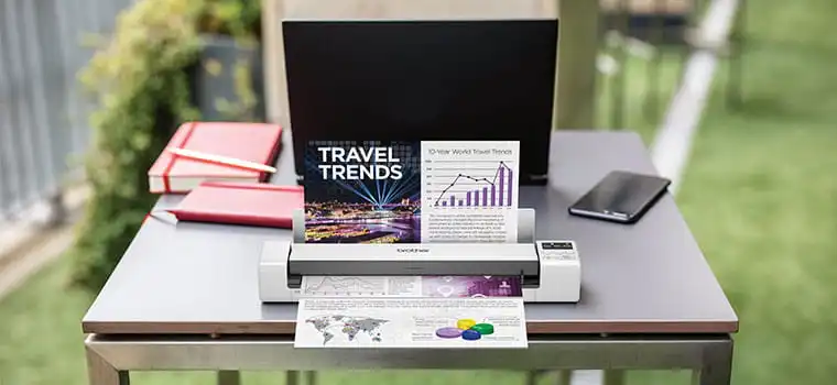 Brother DS-620 Portable document scanner scanning a colour document on table, laptop, orange notebook, mobile phone, grass, outdoors