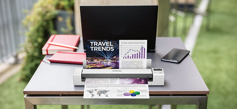 Brother DS-620 Portable document scanner scanning a colour document on table, laptop, orange notebook, mobile phone, grass, outdoors