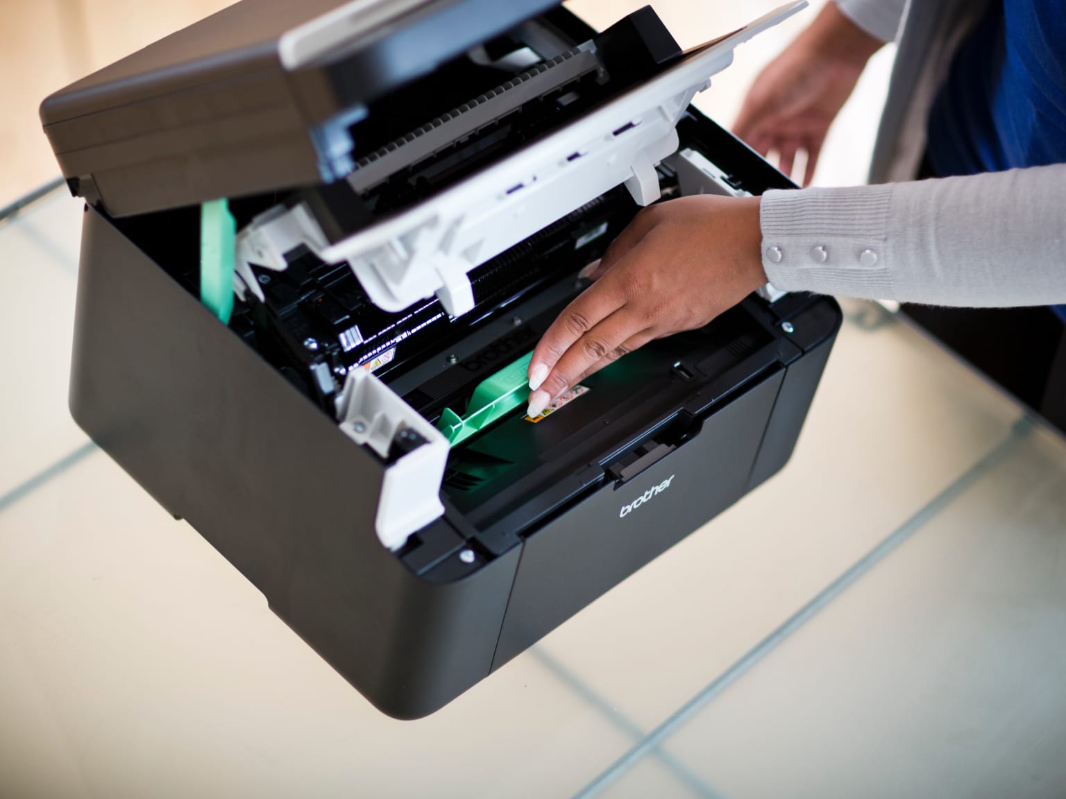 A lady inserting a toner cartridge into a laser printer, revealing the inner workings