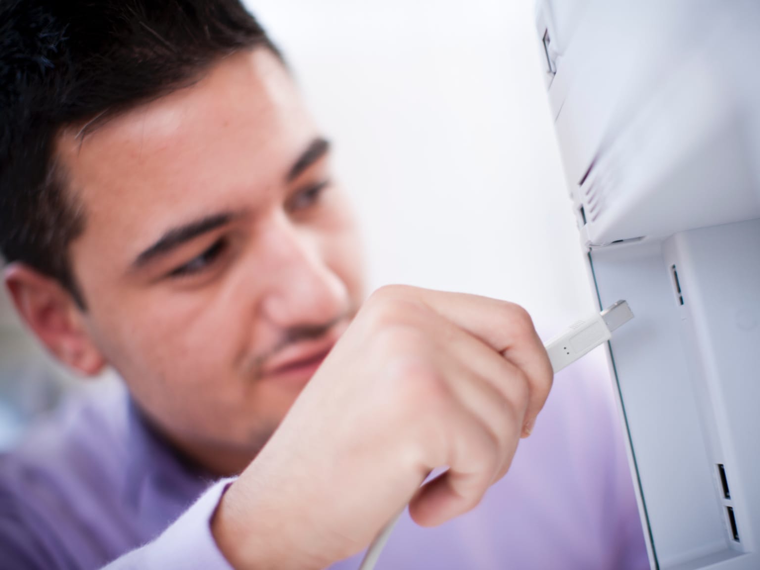 A man inserting a network cable into an ethernet port on the back of a printer